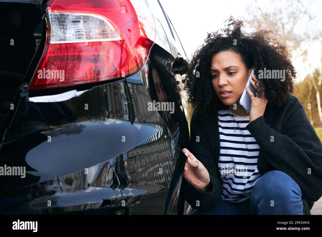 Giovane donna arrabbiata in piedi da auto vandalized nel parcheggio auto segnalazione di danni alla compagnia assicurativa utilizzando il telefono cellulare Foto Stock