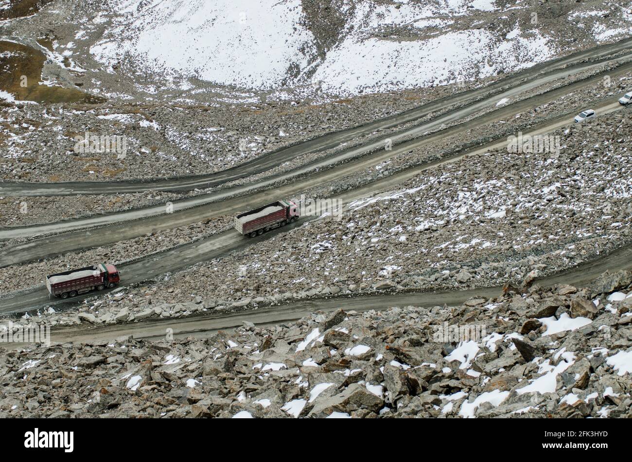 I camion pesanti e gli autocarri articolati navigano lungo l'autostrada G216 non asfaltata che collega Urumuqi alla prefettura di Bayingolin attraverso le montagne innevate di Tianshan a Xinjiang, Cina, RPC. © Time-Snap Foto Stock