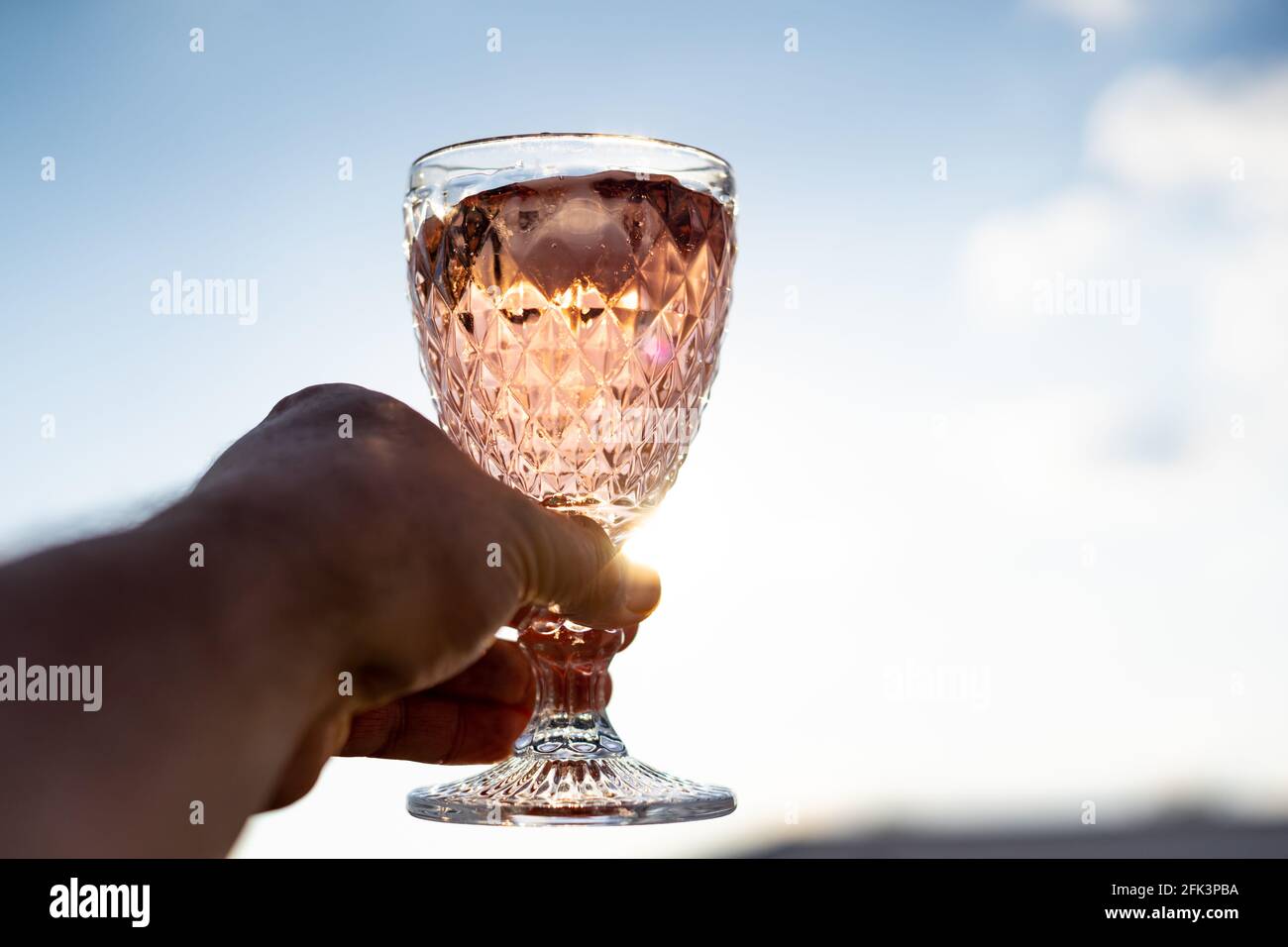 Tenere a mano un bicchiere elegante con un cocktail rosa il sole Foto Stock