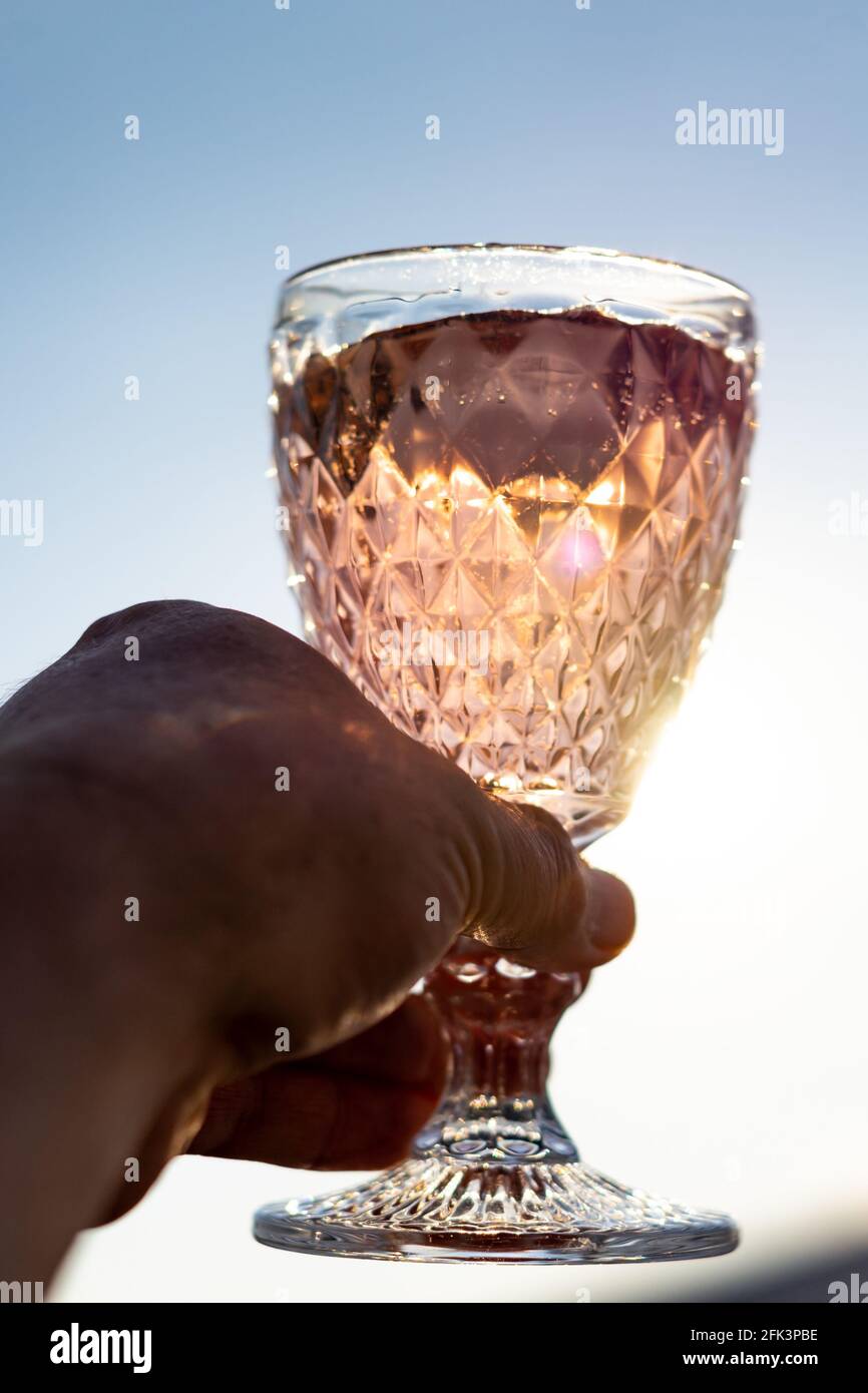 Tenere a mano un bicchiere elegante con un cocktail rosa il sole Foto Stock
