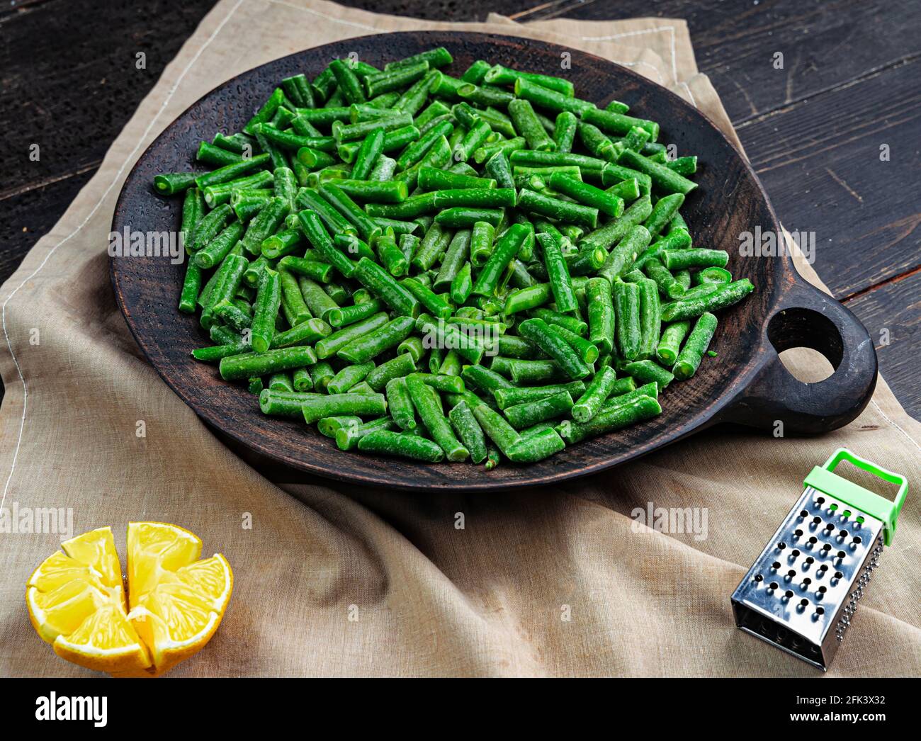 Fagioli verdi in una piastra di legno. Cialde verdi tagliate fresche Foto Stock