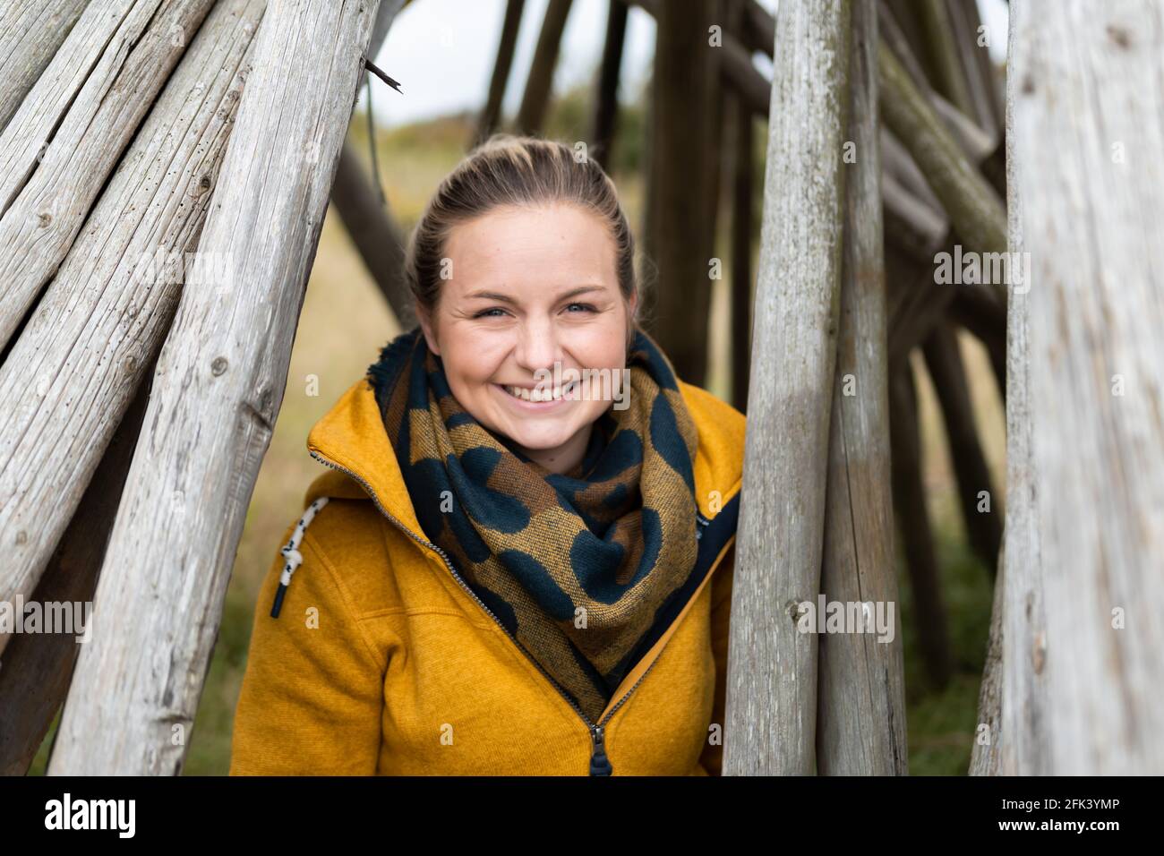 Bella donna bionda in camice giallo in piedi tra tronchi di legno in un porto di fiordo in danimarca Foto Stock