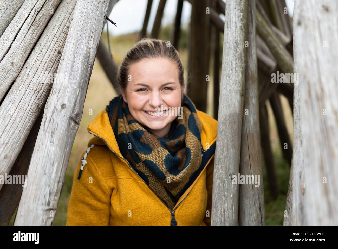Bella donna bionda in camice giallo in piedi tra tronchi di legno in un porto di fiordo in danimarca Foto Stock