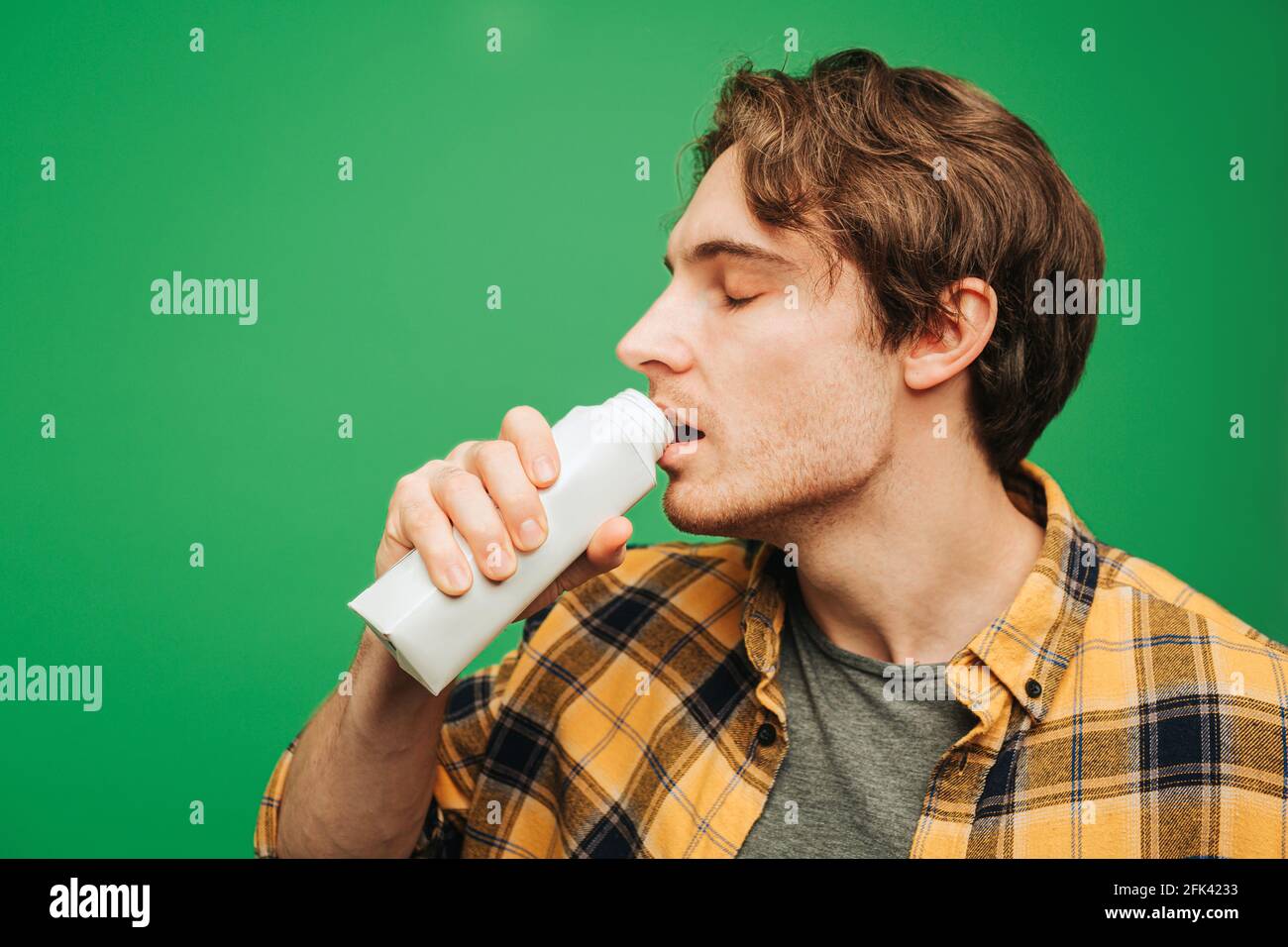 Il giovane beve il latte con piacere, isolato su sfondo verde Foto Stock
