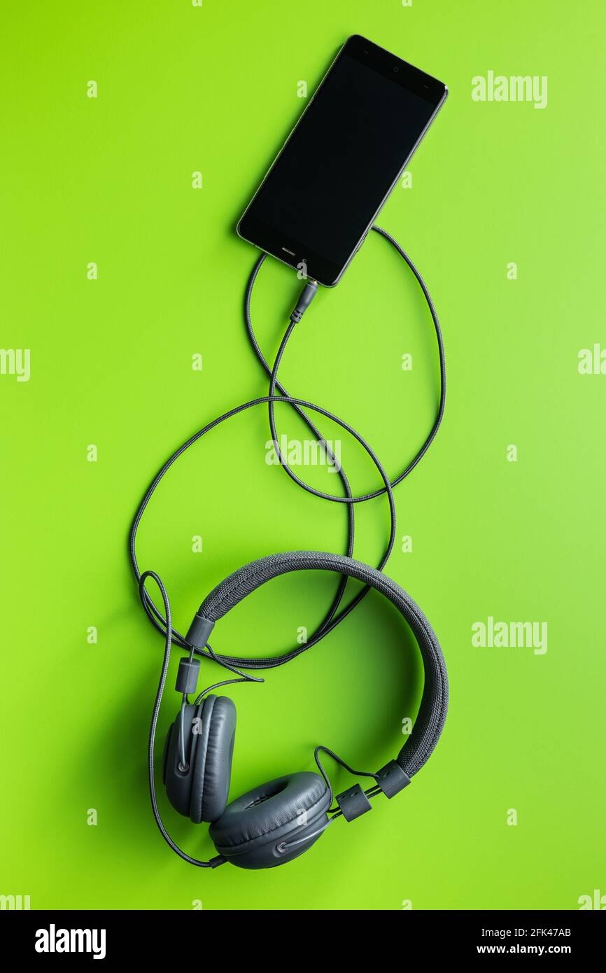 Cuffie stereo cablate collegate allo smartphone su sfondo verde. Vista dall'alto. Foto Stock