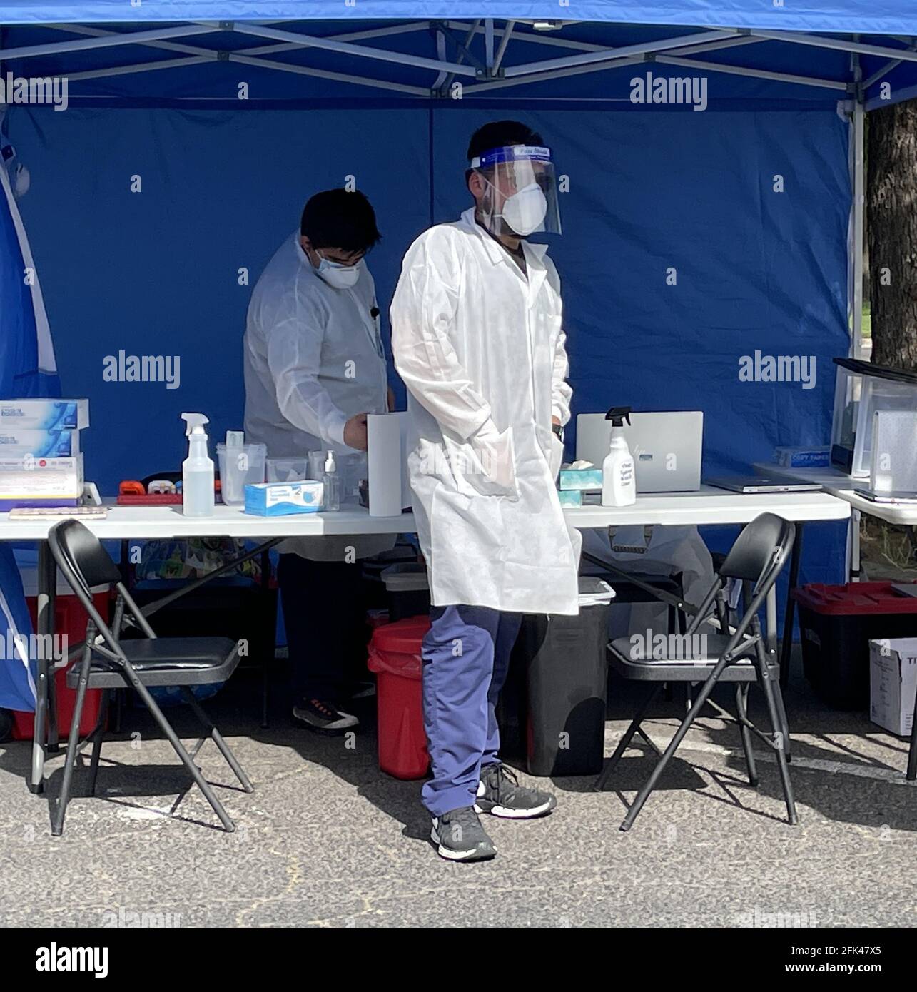 Tecnico medico che dà i colpi di Covid all'esterno indossando una maschera facciale e un camice da laboratorio Foto Stock