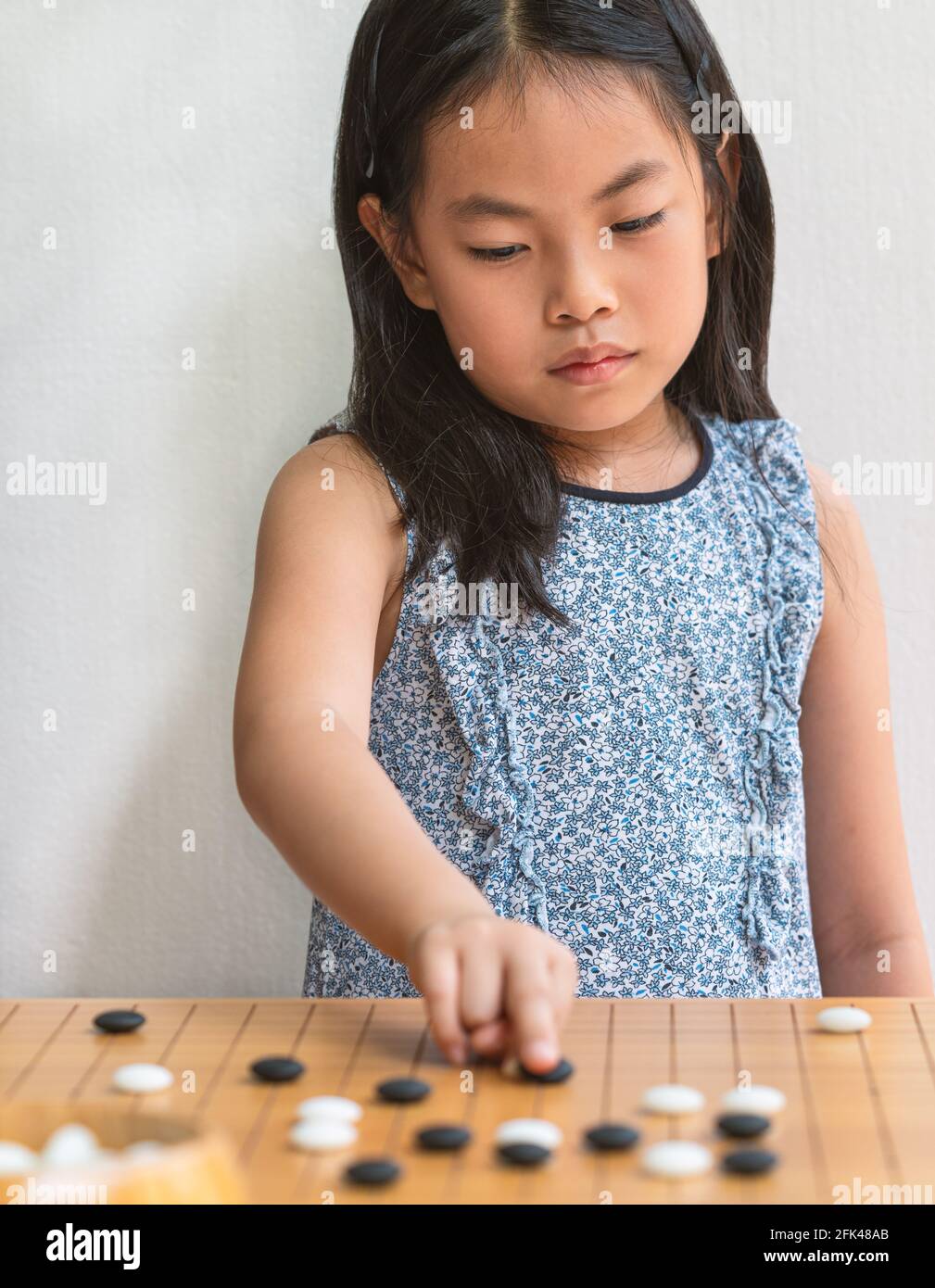 Ritratto Asian bambina ragazza gioca Go, il gioco da tavolo giapponese o cinese, mettere a fuoco sul gioco da tavolo, parete bianca, immagine verticale. Foto Stock