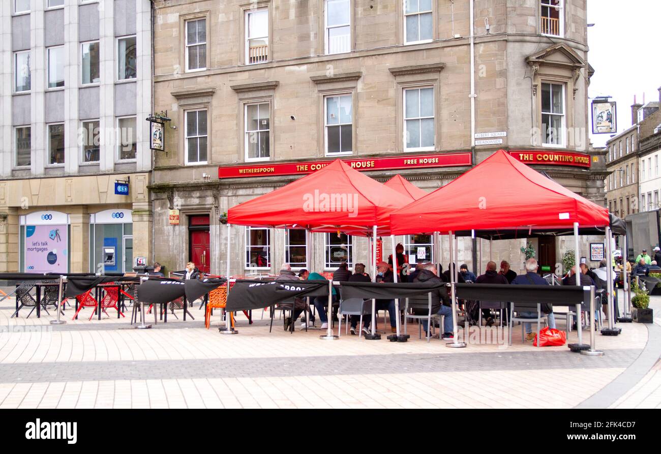 Dundee, Tayside, Scozia, Regno Unito. 28 aprile 2021. Regno Unito tempo: Freddo pomeriggio luminoso attraverso la Scozia nord-orientale con temperature che raggiungono i 9°C. I pub scozzesi hanno finalmente riaperto dopo mesi di rigide restrizioni di blocco del Covid-19. Il governo della Scozia ha permesso alle case pubbliche di tutto il paese di riaprire fino alle 22:00, purché abbiano giardini di birreria all'aperto. I residenti locali approfittano delle nuove norme di blocco e delle condizioni meteorologiche favorevoli per incontrare il pub Wetherspoon`s Counting House per gustare un drink nel centro di Dundee. Credit: Dundee Photographics/Alamy Live Foto Stock