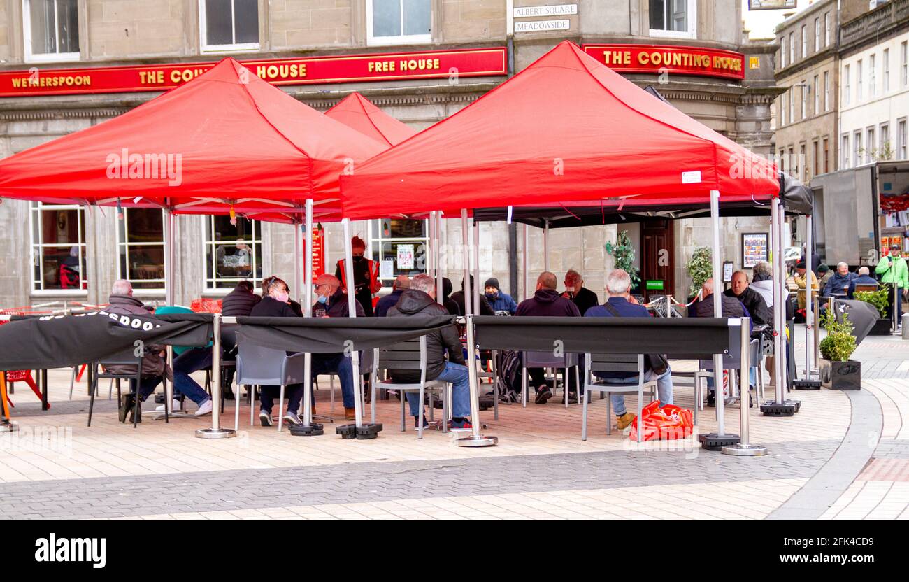 Dundee, Tayside, Scozia, Regno Unito. 28 aprile 2021. Regno Unito tempo: Freddo pomeriggio luminoso attraverso la Scozia nord-orientale con temperature che raggiungono i 9°C. I pub scozzesi hanno finalmente riaperto dopo mesi di rigide restrizioni di blocco del Covid-19. Il governo della Scozia ha permesso alle case pubbliche di tutto il paese di riaprire fino alle 22:00, purché abbiano giardini di birreria all'aperto. I residenti locali approfittano delle nuove norme di blocco e delle condizioni meteorologiche favorevoli per incontrare il pub Wetherspoon`s Counting House per gustare un drink nel centro di Dundee. Credit: Dundee Photographics/Alamy Live Foto Stock