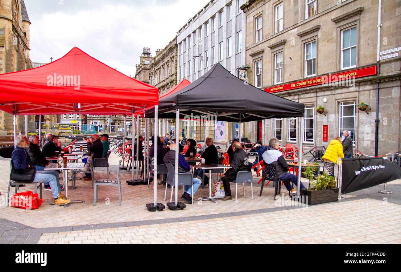 Dundee, Tayside, Scozia, Regno Unito. 28 aprile 2021. Regno Unito tempo: Freddo pomeriggio luminoso attraverso la Scozia nord-orientale con temperature che raggiungono i 9°C. I pub scozzesi hanno finalmente riaperto dopo mesi di rigide restrizioni di blocco del Covid-19. Il governo della Scozia ha permesso alle case pubbliche di tutto il paese di riaprire fino alle 22:00, purché abbiano giardini di birreria all'aperto. I residenti locali approfittano delle nuove norme di blocco e delle condizioni meteorologiche favorevoli per incontrare il pub Wetherspoon`s Counting House per gustare un drink nel centro di Dundee. Credit: Dundee Photographics/Alamy Live Foto Stock
