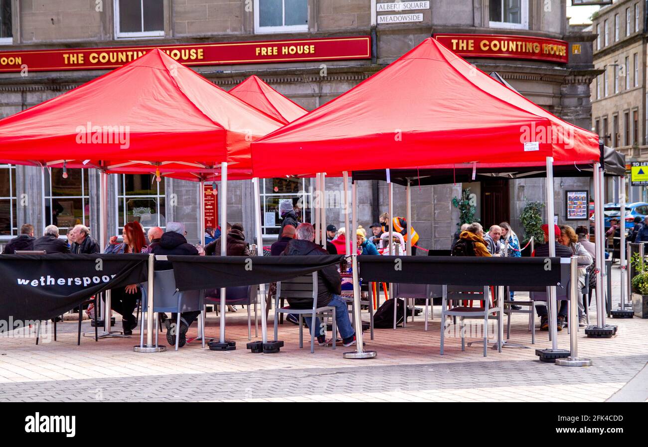 Dundee, Tayside, Scozia, Regno Unito. 28 aprile 2021. Regno Unito tempo: Freddo pomeriggio luminoso attraverso la Scozia nord-orientale con temperature che raggiungono i 9°C. I pub scozzesi hanno finalmente riaperto dopo mesi di rigide restrizioni di blocco del Covid-19. Il governo della Scozia ha permesso alle case pubbliche di tutto il paese di riaprire fino alle 22:00, purché abbiano giardini di birreria all'aperto. I residenti locali approfittano delle nuove norme di blocco e delle condizioni meteorologiche favorevoli per incontrare il pub Wetherspoon`s Counting House per gustare un drink nel centro di Dundee. Credit: Dundee Photographics/Alamy Live Foto Stock
