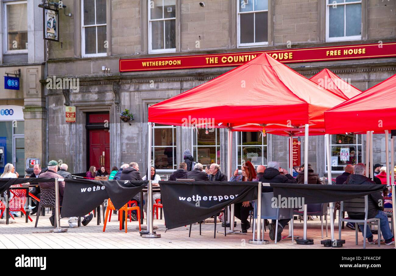 Dundee, Tayside, Scozia, Regno Unito. 28 aprile 2021. Regno Unito tempo: Freddo pomeriggio luminoso attraverso la Scozia nord-orientale con temperature che raggiungono i 9°C. I pub scozzesi hanno finalmente riaperto dopo mesi di rigide restrizioni di blocco del Covid-19. Il governo della Scozia ha permesso alle case pubbliche di tutto il paese di riaprire fino alle 22:00, purché abbiano giardini di birreria all'aperto. I residenti locali approfittano delle nuove norme di blocco e delle condizioni meteorologiche favorevoli per incontrare il pub Wetherspoon`s Counting House per gustare un drink nel centro di Dundee. Credit: Dundee Photographics/Alamy Live Foto Stock