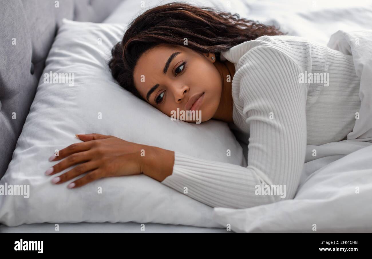 Donna nera depressa giacente a letto da sola e sconvolto Foto Stock