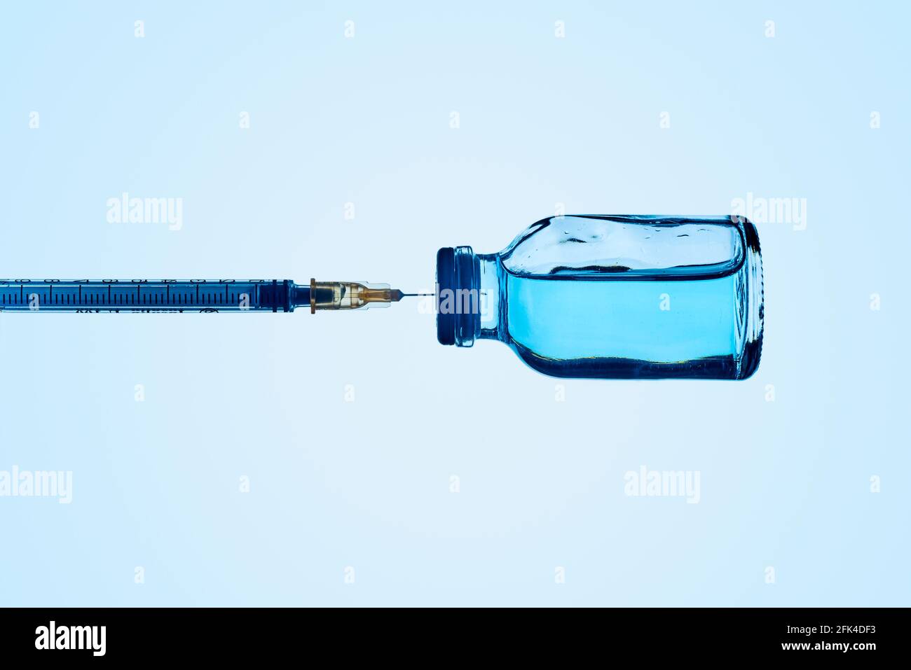 una siringa in un flaconcino di vaccino con un liquido blu, su sfondo blu Foto Stock