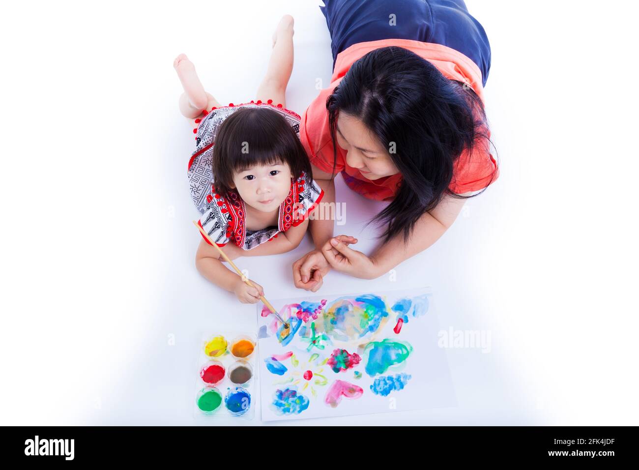 Ritratto di piccola ragazza asiatica (tailandese) pittura e utilizzando strumenti di pittura (vernici acquerello, pennello) con sua madre vicino, su sfondo bianco. C Foto Stock