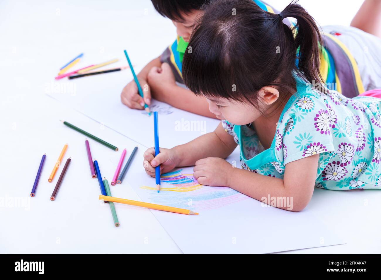 I fratelli asiatici (thailandesi) si trovano sul pavimento e disegnano su carta, su sfondo bianco. I concetti di creatività e di educazione, rafforzano l'immaginazione di c Foto Stock