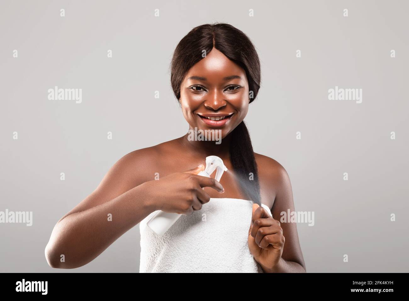 Cura quotidiana dei capelli. Ritratto di sorridente afroamericana femmina applicando Hairspray idratante Foto Stock