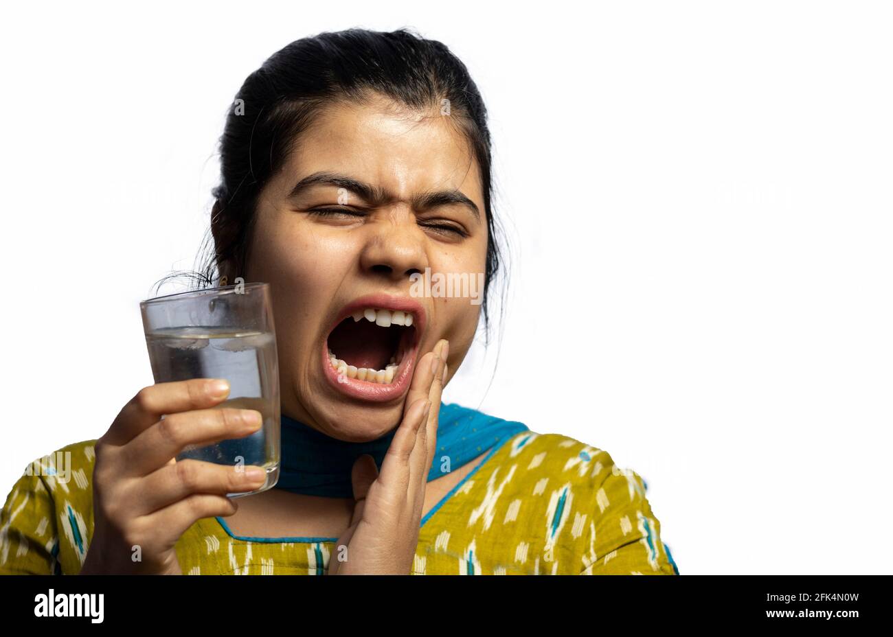 Una donna indiana asiatica con un bicchiere di acqua fredda toccando la guancia che mostra sensibilità ai denti su sfondo bianco Foto Stock