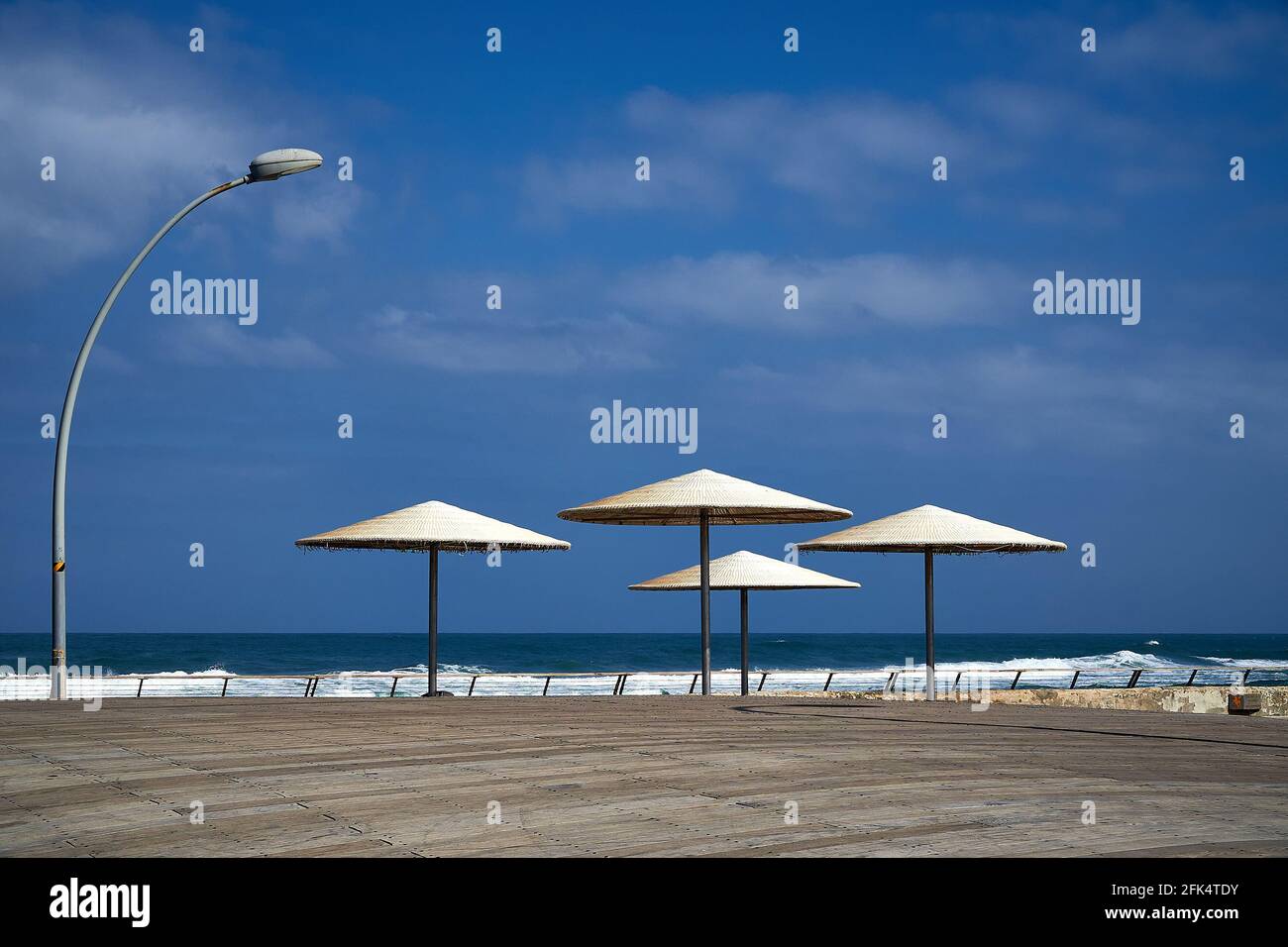 Ombrelloni da spiaggia e grande lanterna ricurva su una costa marina. Piccolo pezzo di mare e cielo blu con le nuvole. Foto Stock