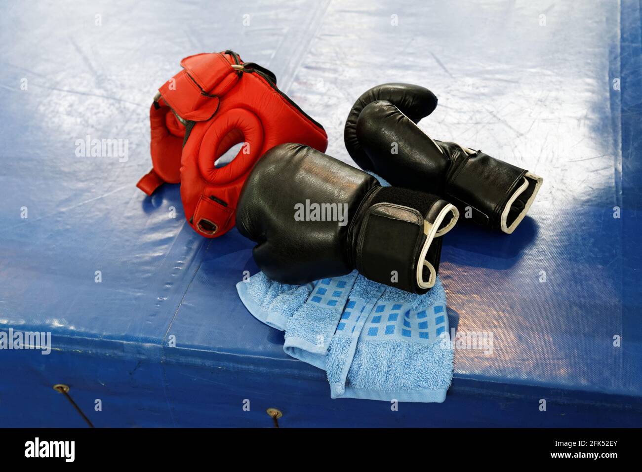 Due guanti da boxe in pelle nera, copricapo protettivo rosso e asciugamano blu si trovano sul bordo dell'anello di boxe Foto Stock