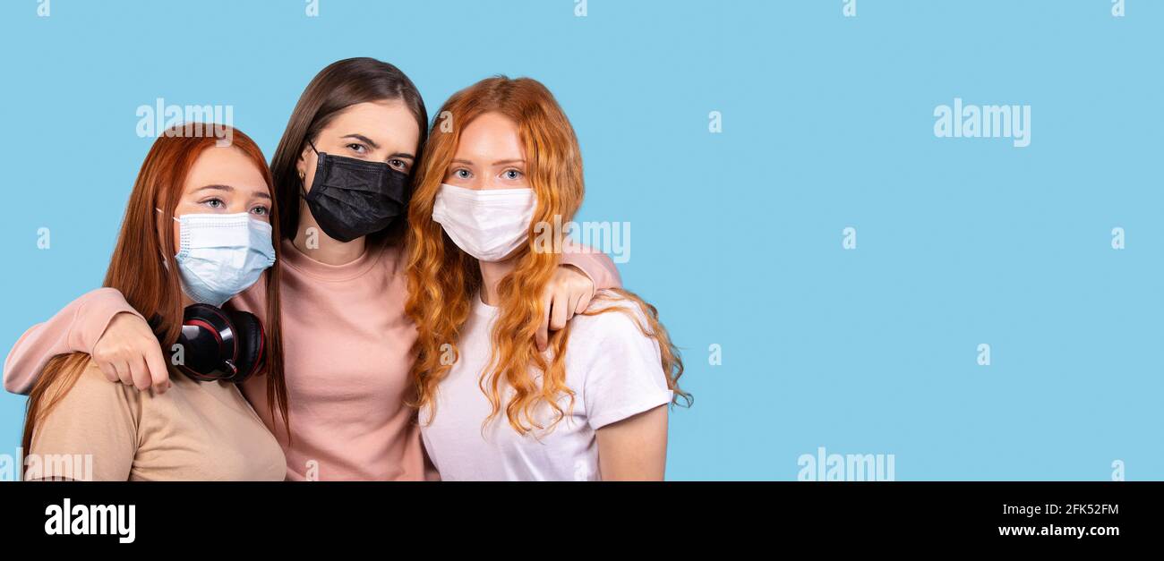 Ritratto di tre amici che indossano maschere protettive su sfondo blu. Foto Stock