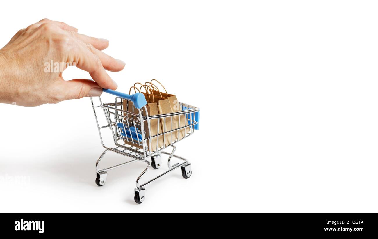 Mano femmina che tiene delicatamente un carrello giocattolo supermercato con borse di carta per la spesa. Isolato su bianco. Concetto di shopping, vendita, Black Friday, Cyber Monda Foto Stock