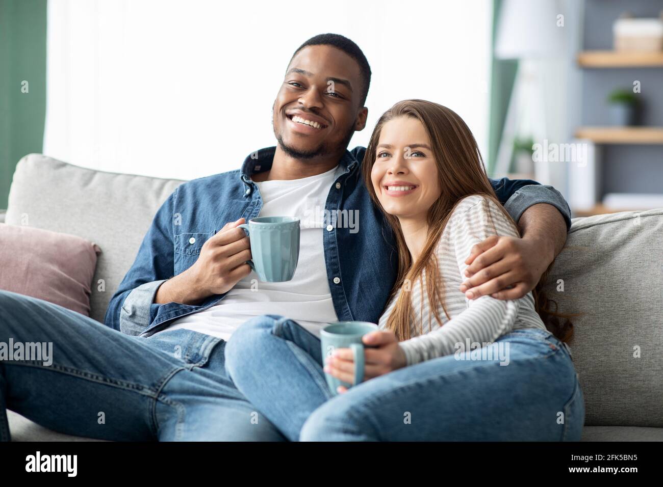 Fine settimana nazionale. Felice coppia multiculturale guardare la tv e bere caffè a casa Foto Stock