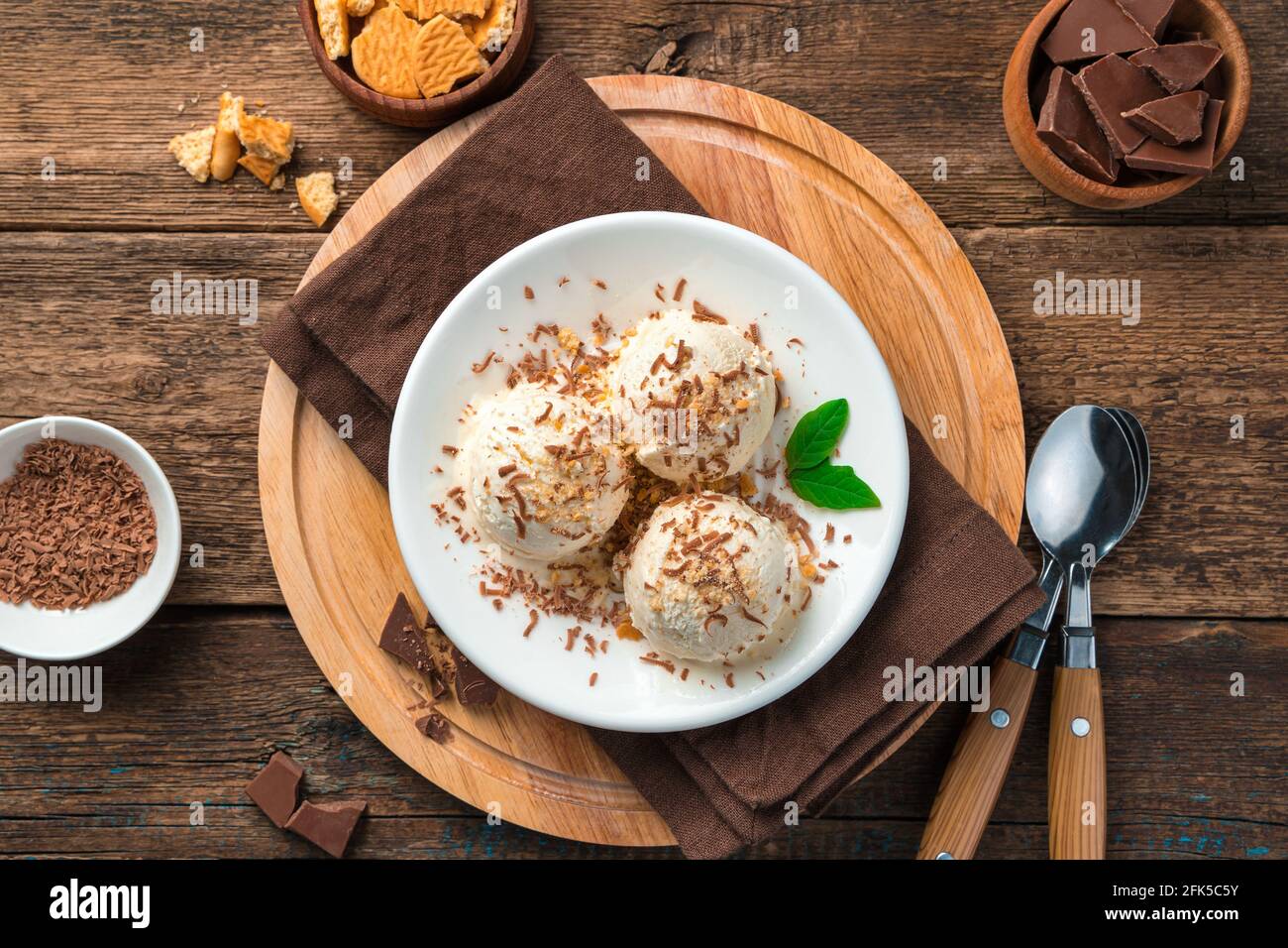 Dessert alla vaniglia freddo e cremoso con cioccolato e menta su sfondo marrone. Palle di gelato. Foto Stock