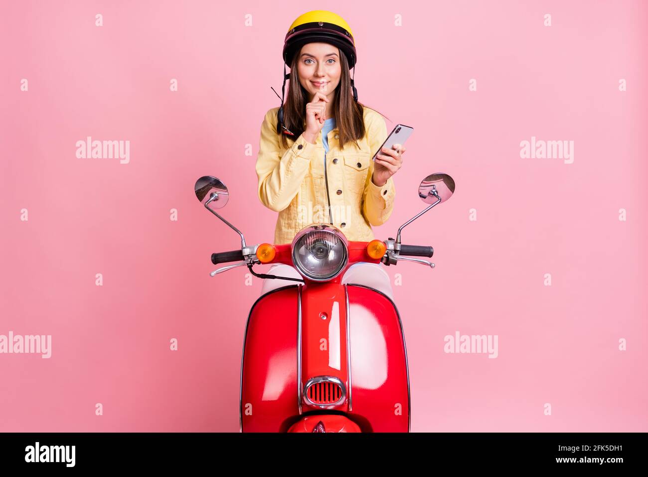 Foto di giovane allegra bella ragazza womanl tenere la mano del telefono chin ride moto rosso isolato su sfondo rosa Foto Stock