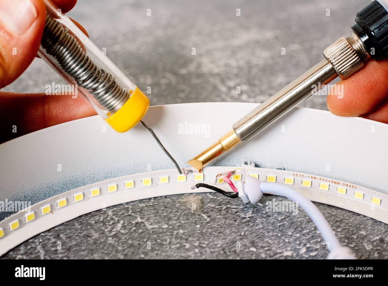 Dettaglio di un saldatore in stagno che ripara una striscia di luci a LED danneggiata. Foto Stock