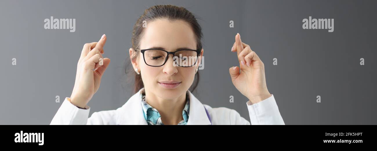 La dottoressa con gli occhi chiusi tiene le dita incrociate Foto Stock