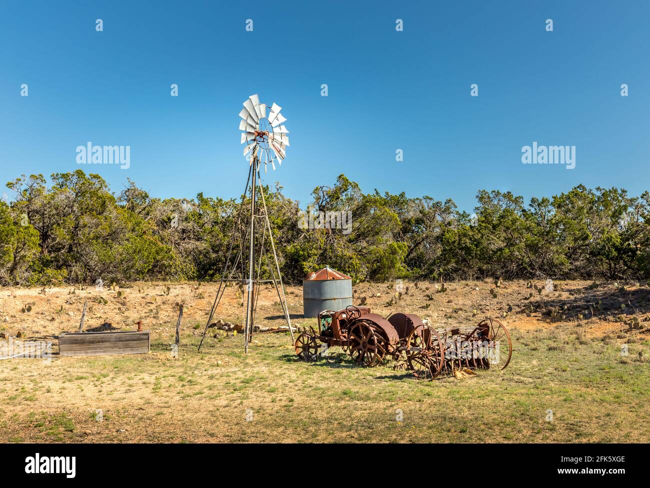 Vecchio trattore arrugginito e un mulino a vento sulle strade secondarie di Texas Foto Stock