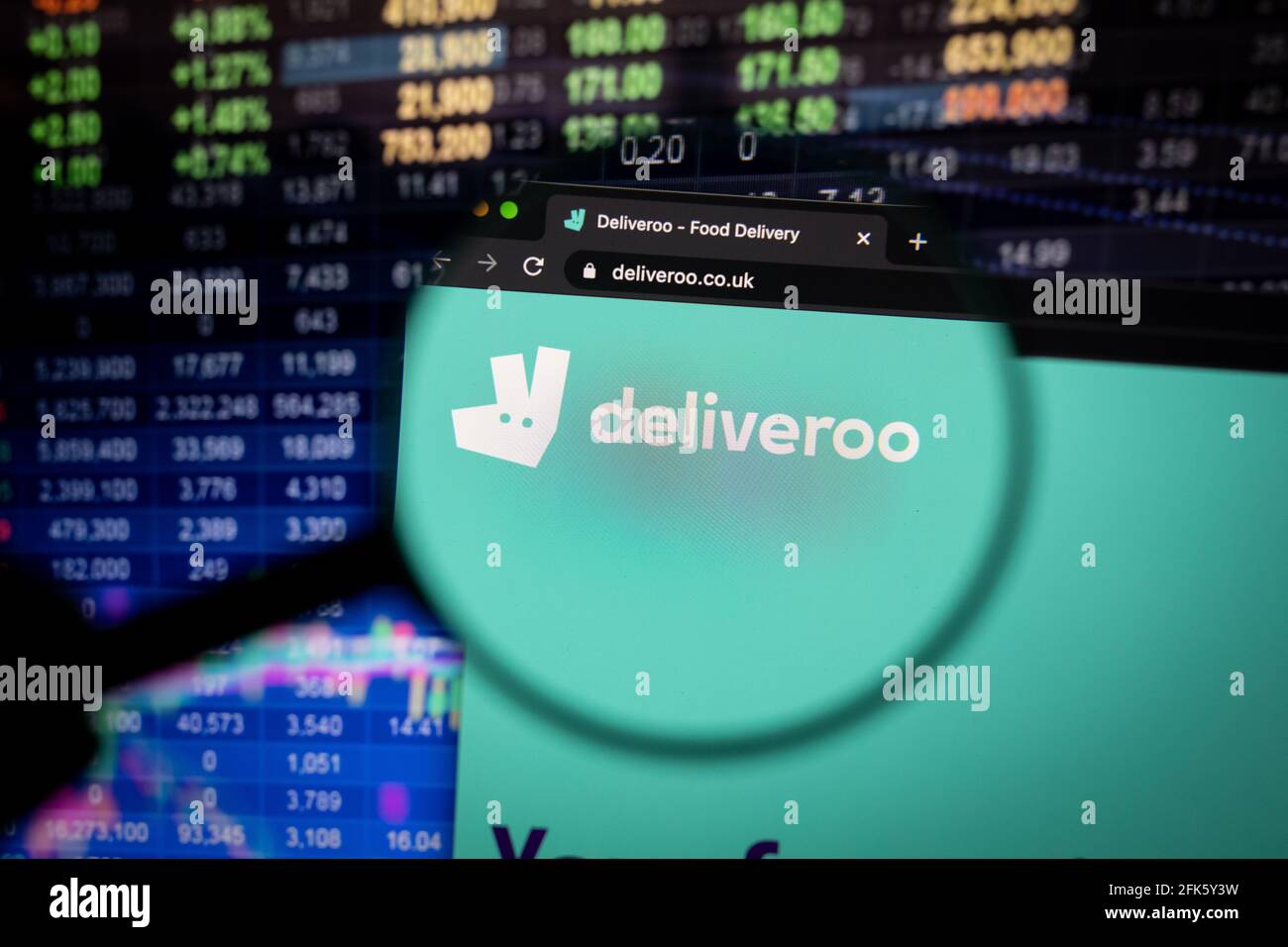 Deliveroo Company logo su un sito web con sviluppi sfocati del mercato azionario in background, visto su uno schermo del computer attraverso una lente di ingrandimento Foto Stock