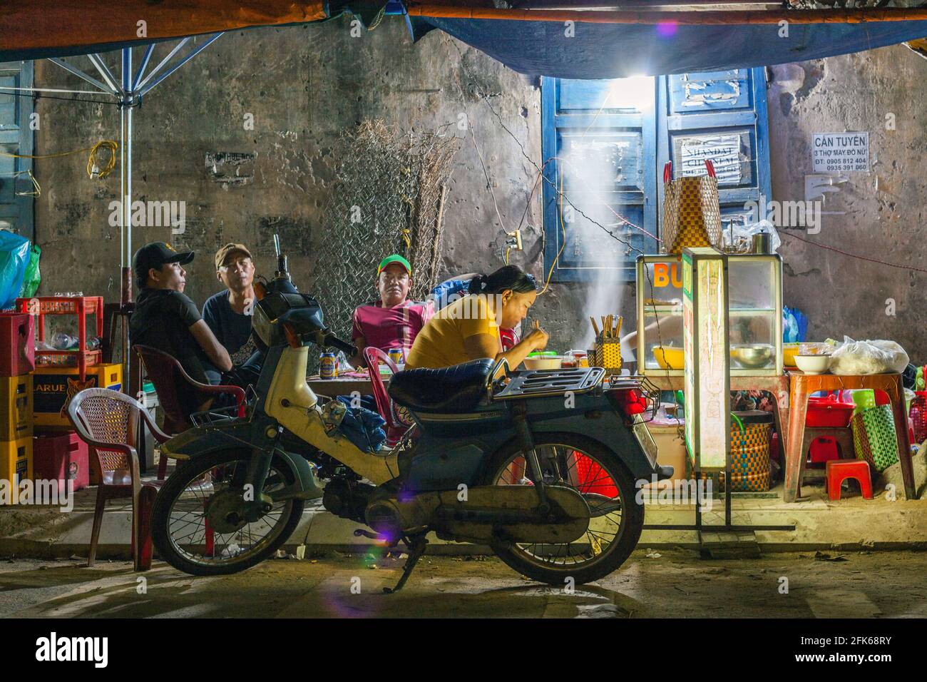 I maschi vietnamiti che si agghiacciano alla bancarella di cibo a bordo strada la sera, Hoi An, Vietnam Foto Stock