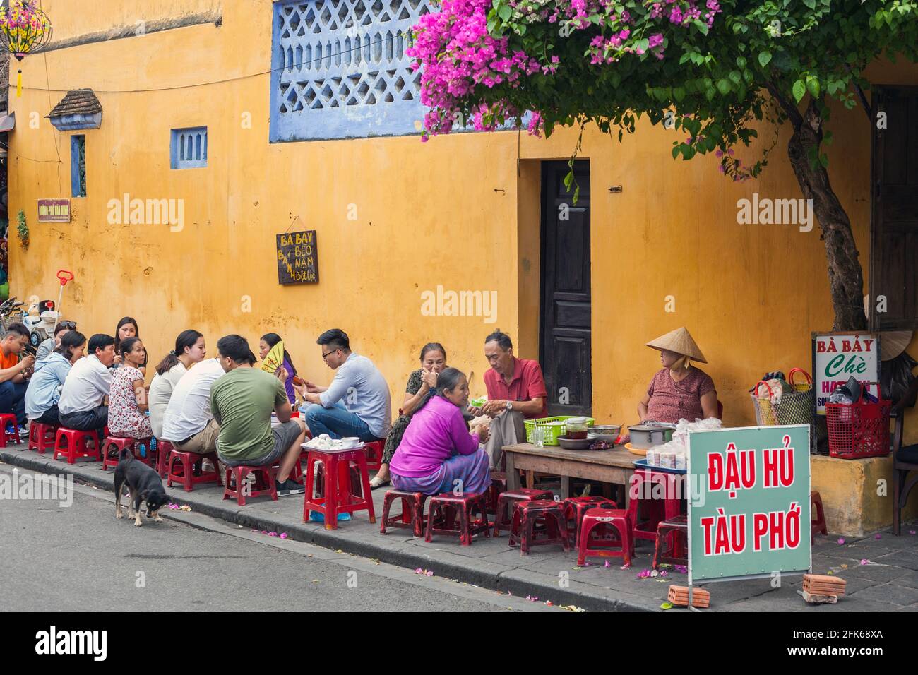 Affollato bar sulla strada nella città vecchia sotto bellissimi fiori bouganville, Hoi An, Vietnam Foto Stock