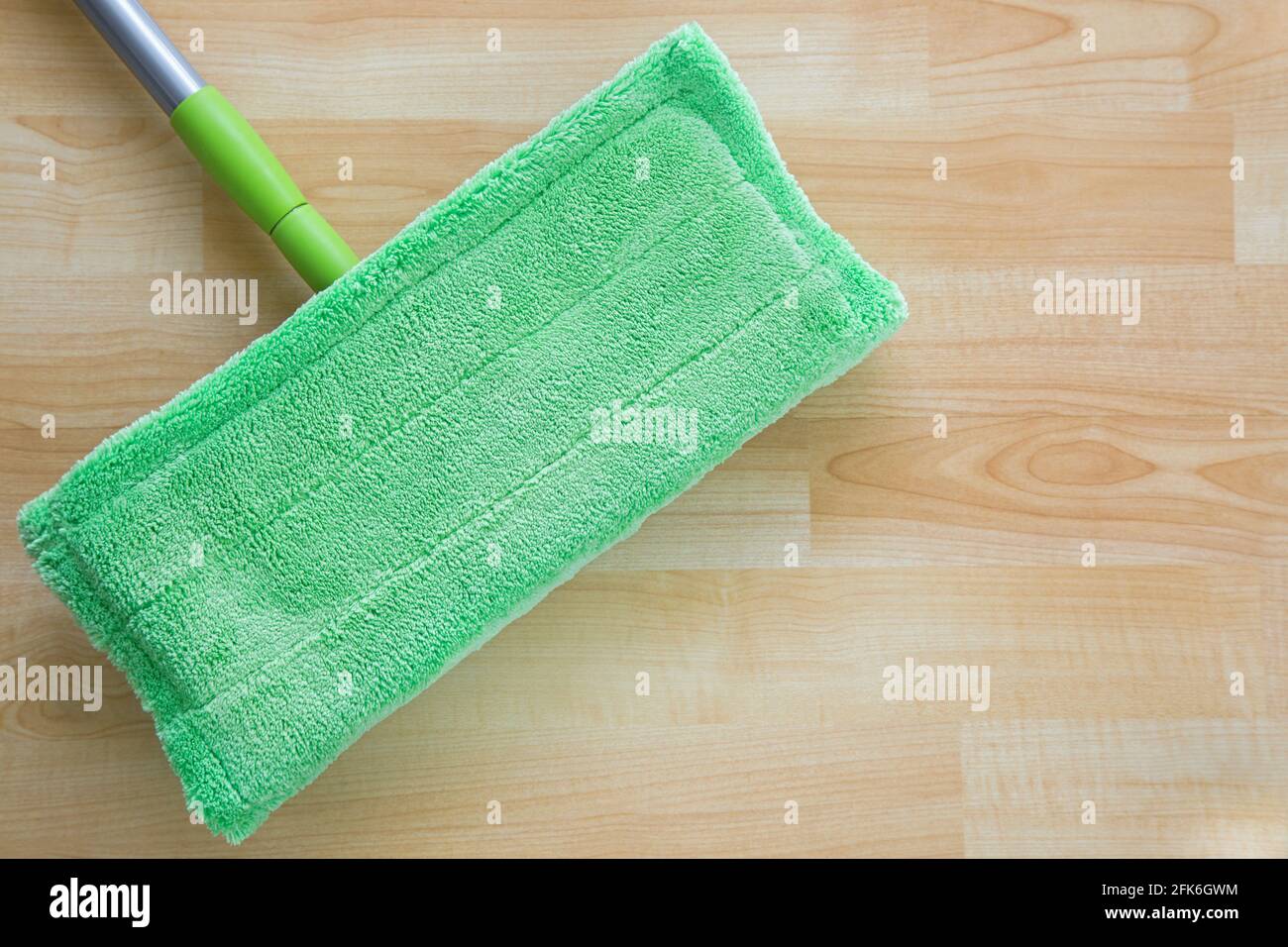 Nuovo spazzolone in microfibra verde pulito per la pulizia del pavimento con manico in argento su pavimento in legno con copyspace Foto Stock