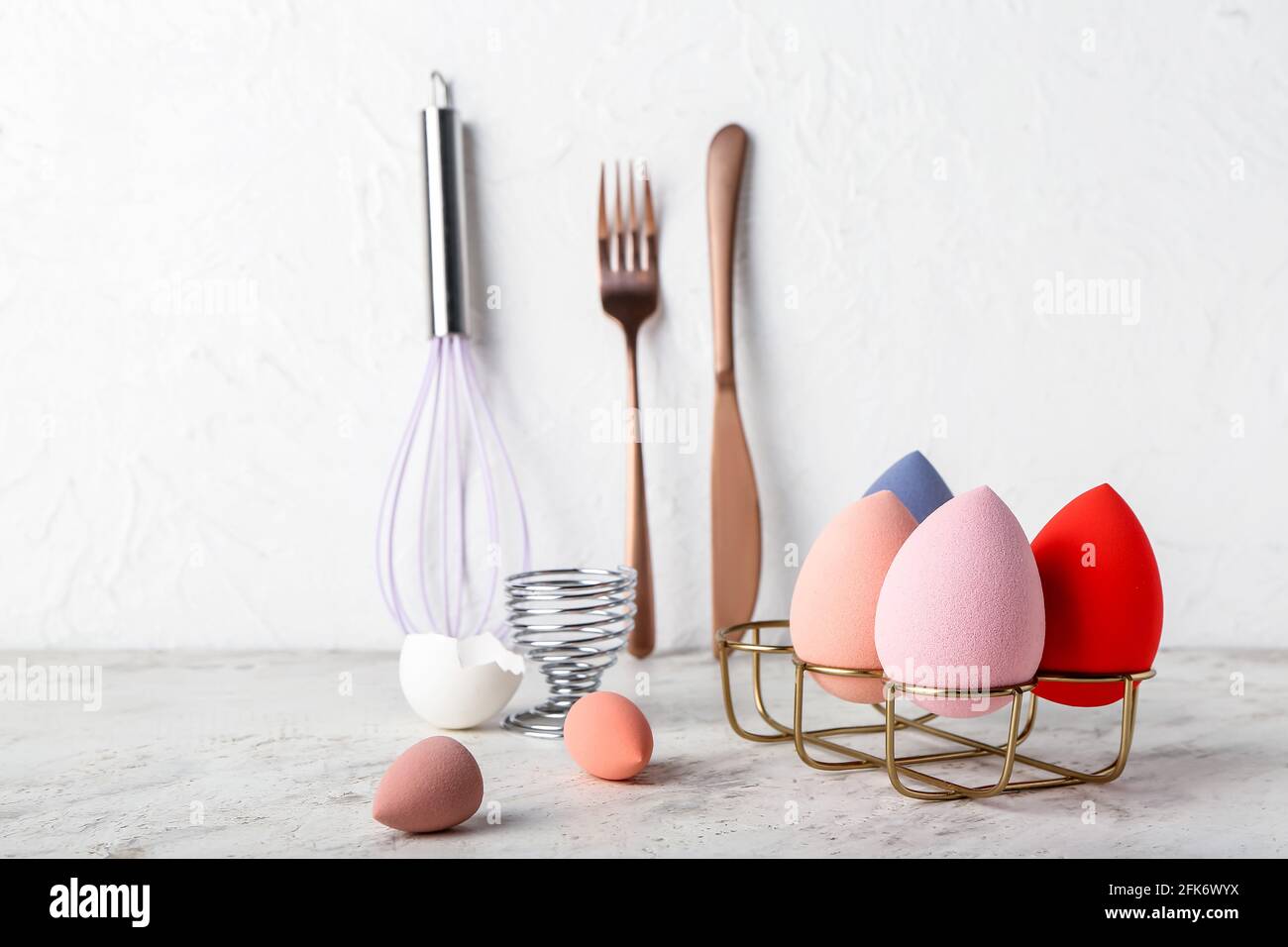 Composizione creativa con spugne per il trucco e utensili da cucina alla luce sfondo Foto Stock