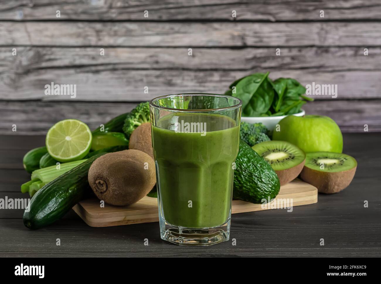Bicchiere di frullato verde organico fresco con spinaci, cetrioli, kiwi, sedano e avocado su sfondo di legno. Foto Stock