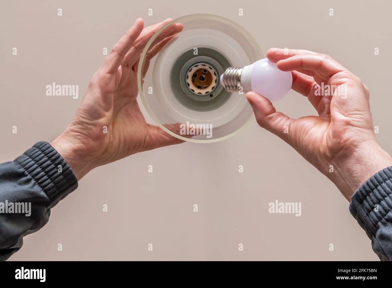 Vista dal basso delle mani di un uomo che è sostituzione di una lampadina al lampadario collegato a. soffitto di una stanza Foto Stock