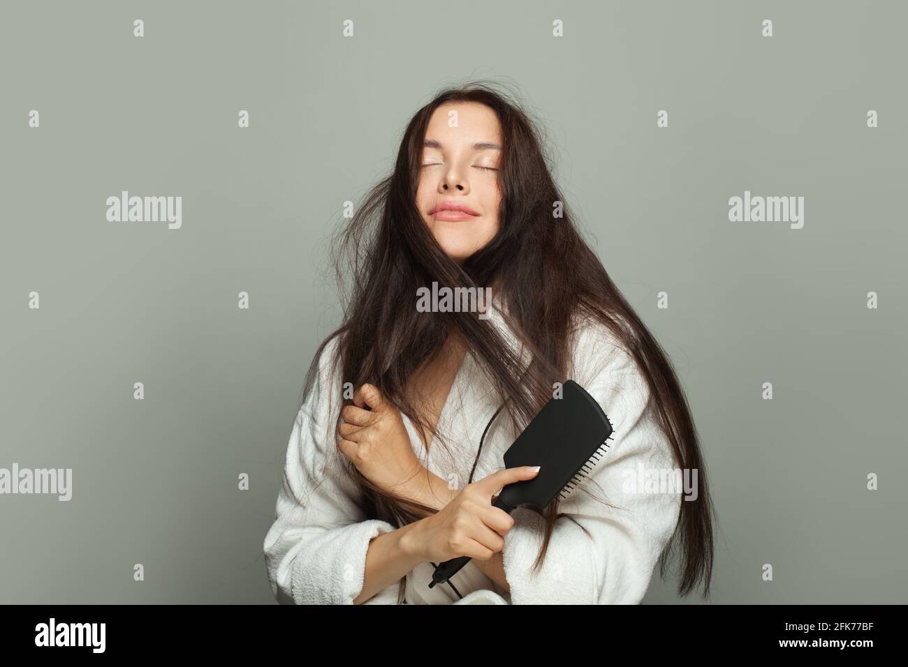 Routine mattutina. Donna carina che combatte i suoi capelli aggrovigliati su sfondo bianco Foto Stock
