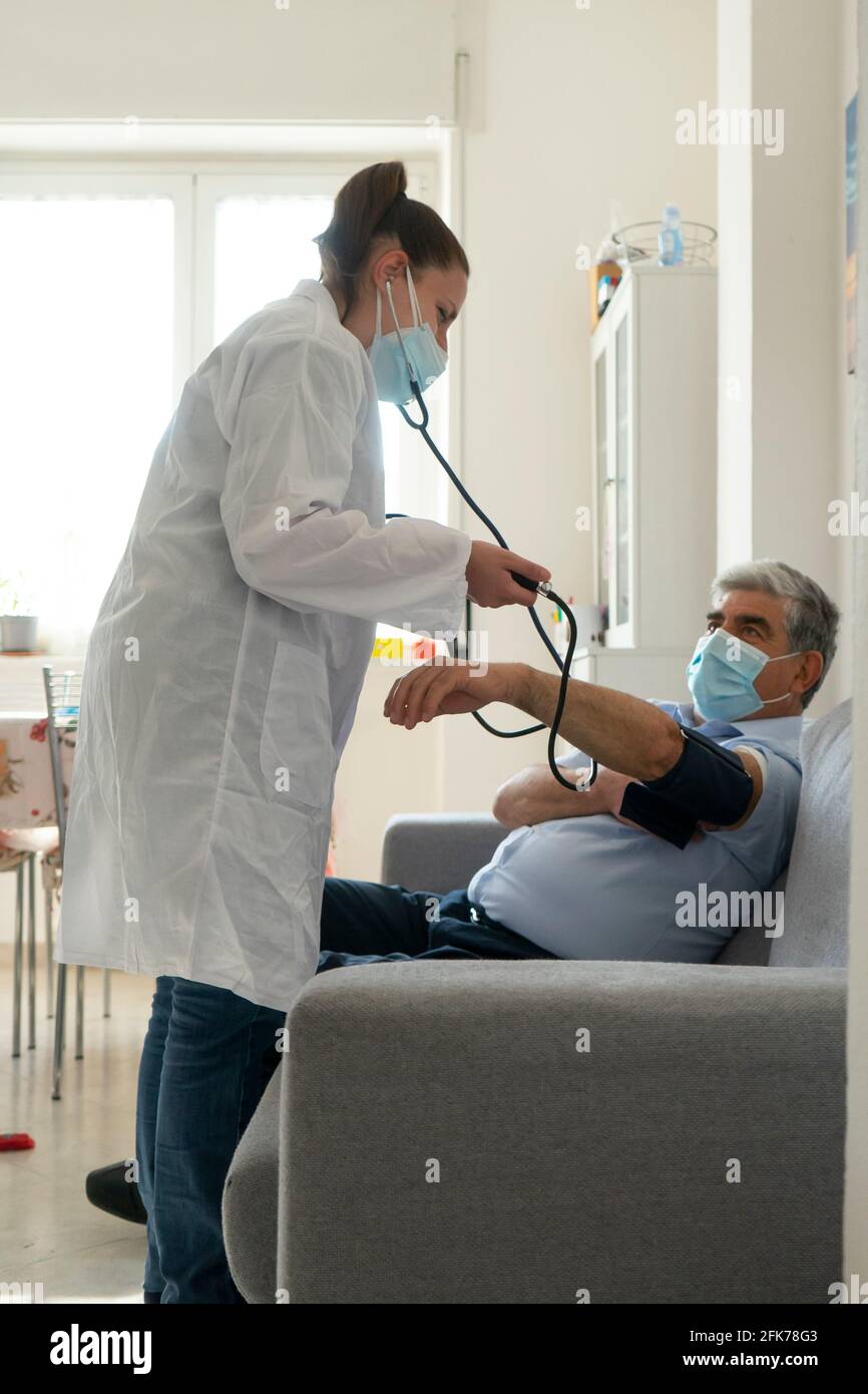 Una giovane dottoressa controlla la pressione sanguigna ad un uomo anziano a casa Foto Stock