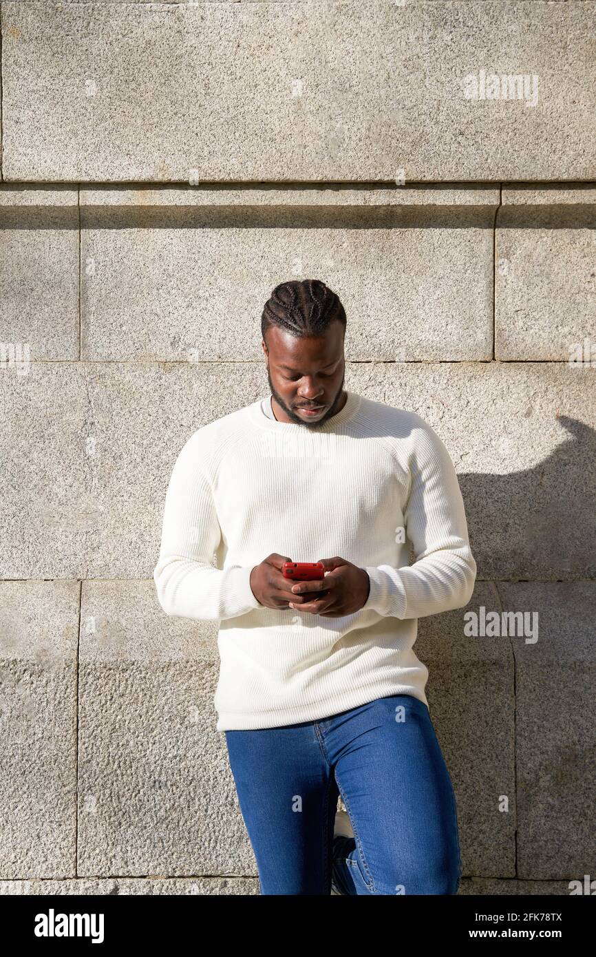 Bell'uomo afro-americano che chiacchiera tramite smartphone in piedi, allegro uomo dalla pelle scura godendo di tempo libero blogging in reti tramite smartphone. Foto di alta qualità Foto Stock