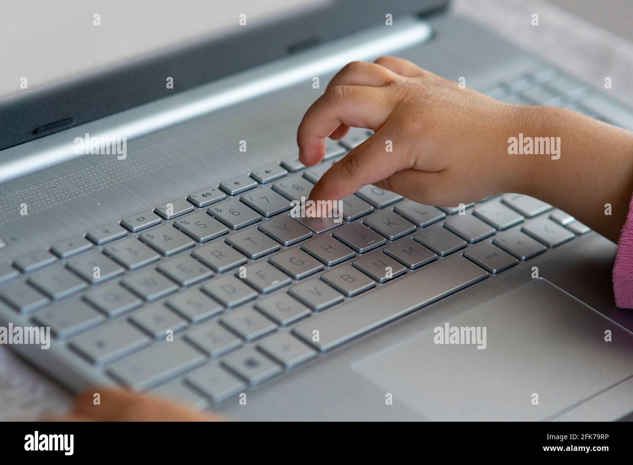 Mano di bambina che usa una tastiera per notebook. Concetto di apprendimento a distanza o di dipendenza informatica e tecnologica dall'infanzia. Foto Stock