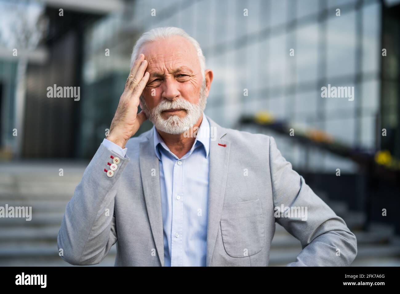 L'uomo d'affari anziano è stanco di lavoro. È in piedi davanti alla costruzione dell'azienda ed ha mal di testa. Foto Stock