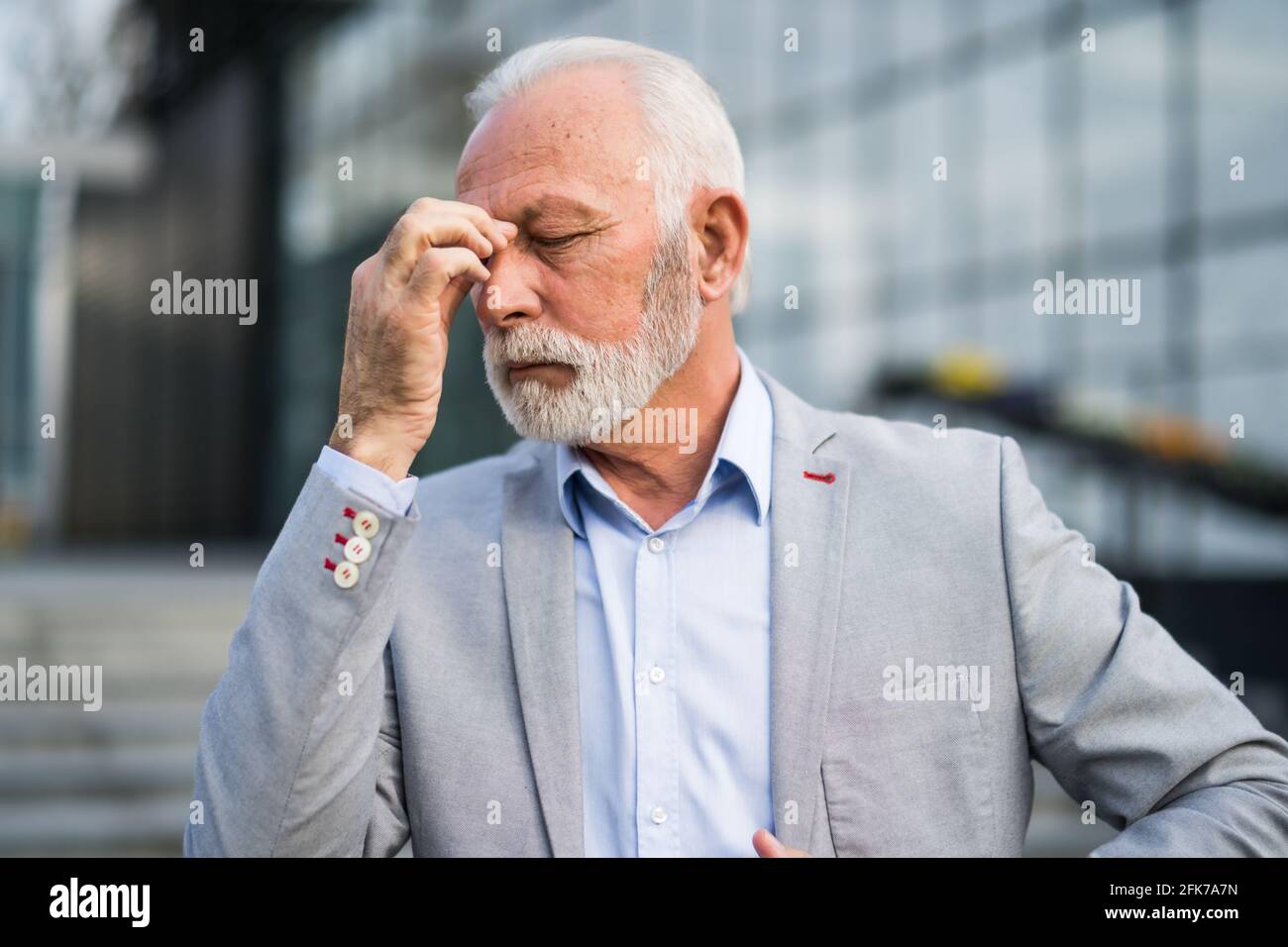 L'uomo d'affari anziano è stanco di lavoro. È in piedi davanti alla costruzione dell'azienda ed ha mal di testa. Foto Stock