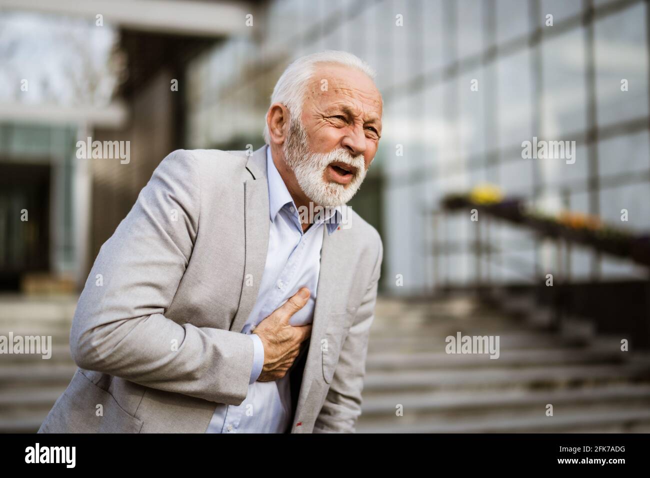 L'uomo d'affari anziano sta avendo colpo davanti alla costruzione dell'azienda. Foto Stock