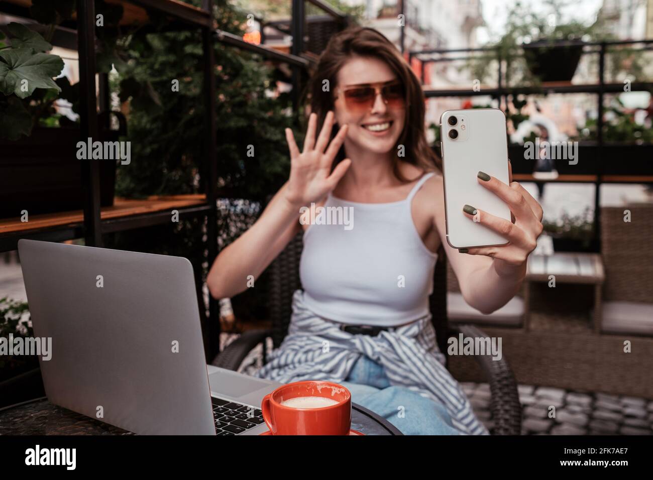 Giovane donna allegra che usa lo smartphone per videochiamare mentre si è seduti In un caffè all'aperto Foto Stock