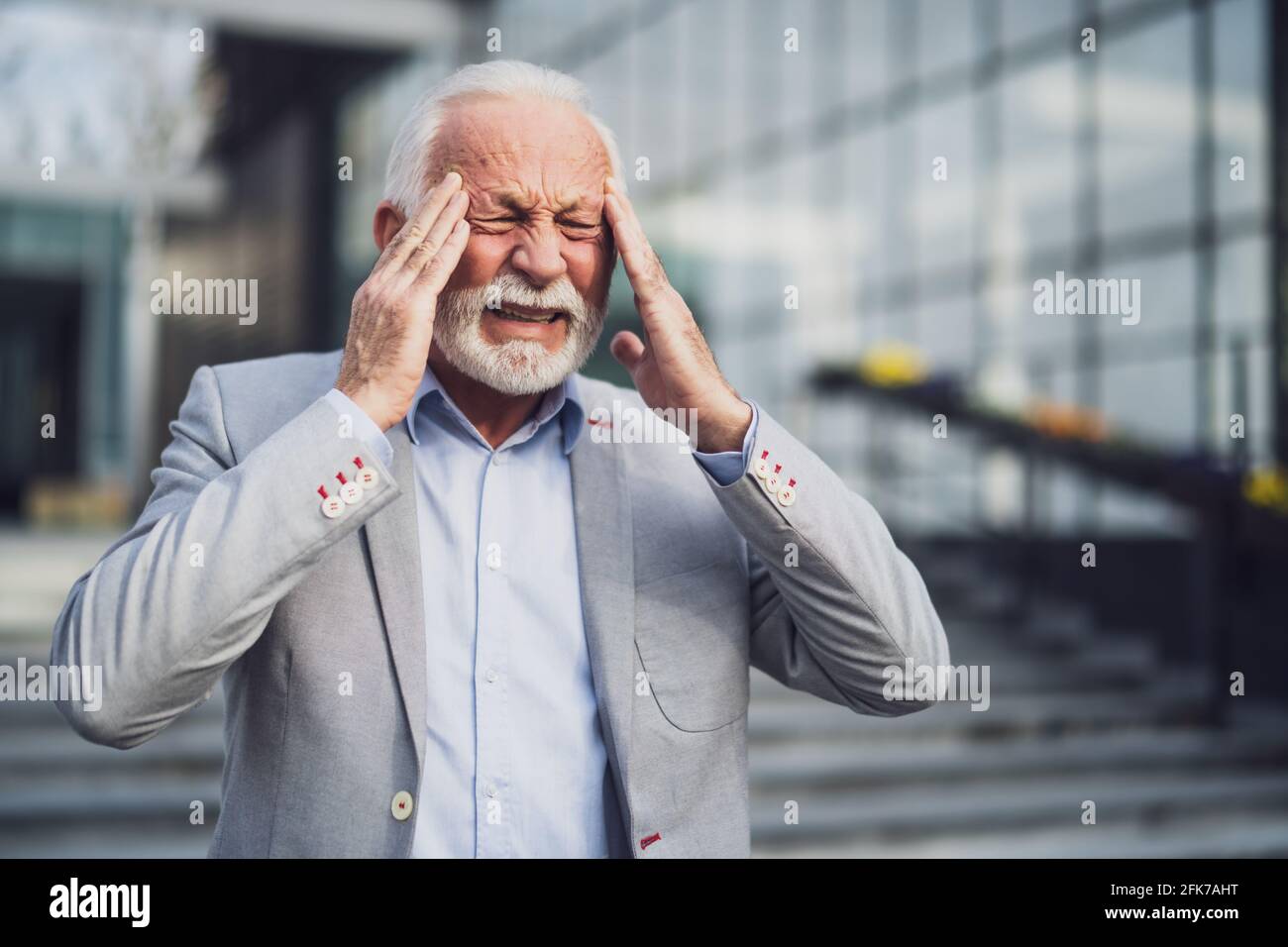 L'uomo d'affari anziano è stanco di lavoro. È in piedi davanti alla costruzione dell'azienda ed ha mal di testa. Foto Stock
