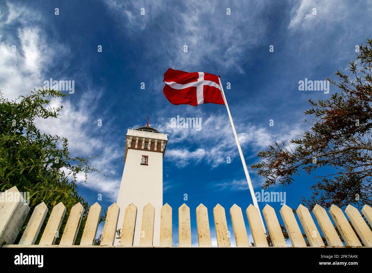 La bandiera danese vola di fronte al faro di Helnaes. Helnæs, Danimarca Foto Stock