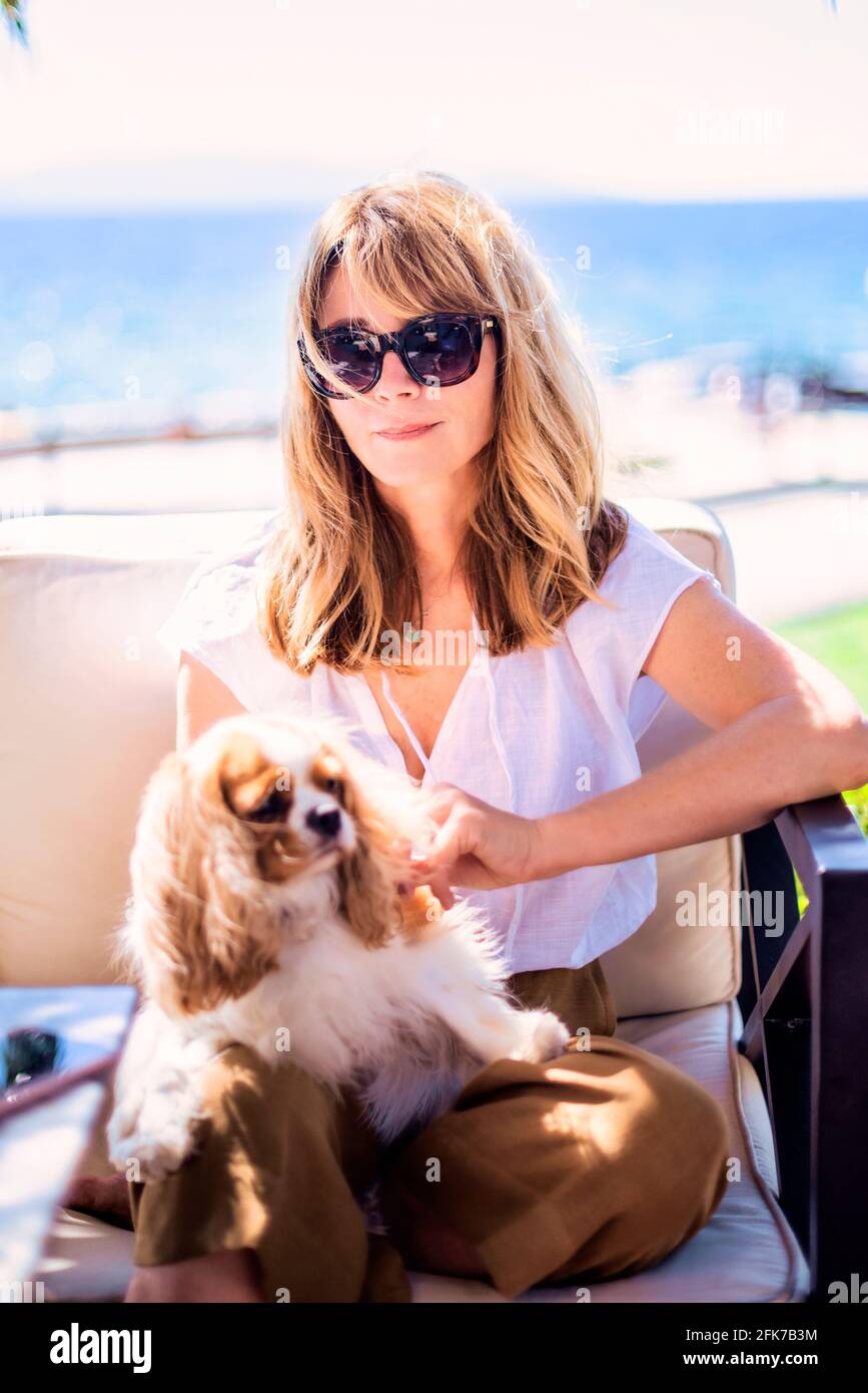 Foto di donna di mezza età godendo di una giornata di sole mentre si rilassa sul mare con simpatico cucciolo. Foto Stock